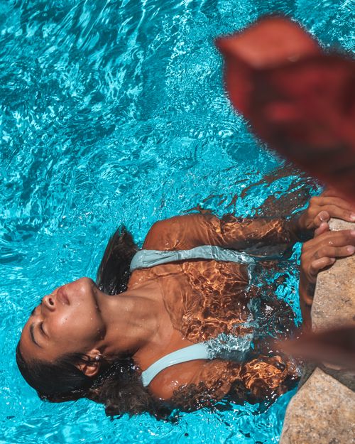 Free Woman enjoying a refreshing swim in a vibrant blue swimming pool on a sunny day. Stock Photo