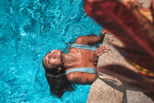 Free A woman in a swimsuit relaxing by the pool on a sunny day. Stock Photo
