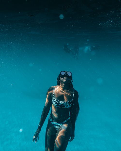Free Stylish woman wearing swimwear and dive mask captured underwater in a vibrant blue ocean. Stock Photo