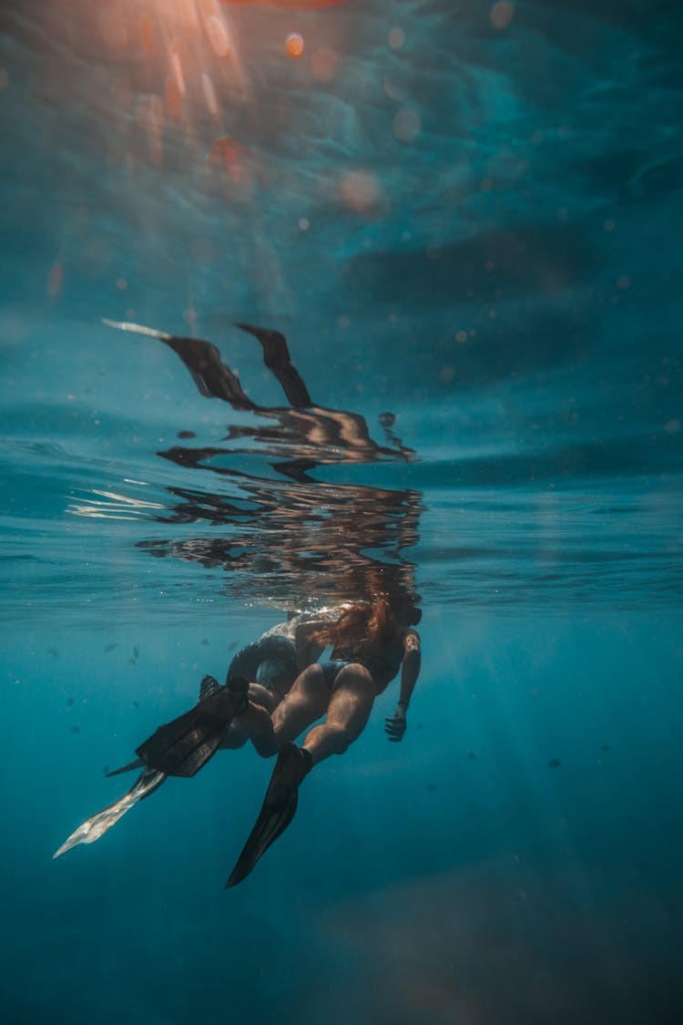 Two People Wearing Flippers Swimming Underwater