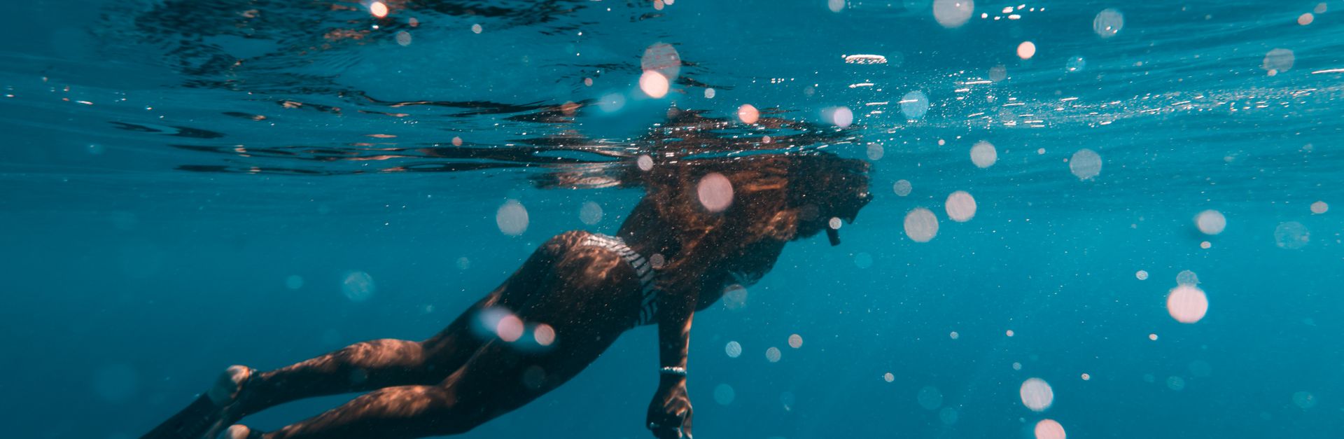 Woman snorkeling underwater, wearing flippers in the clear blue ocean.