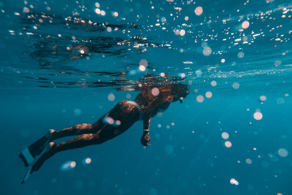 Woman snorkeling underwater, wearing flippers in the clear blue ocean.