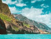 Brown and Green Mountain Beside Blue Sea Under Blue and White Cloudy Sky