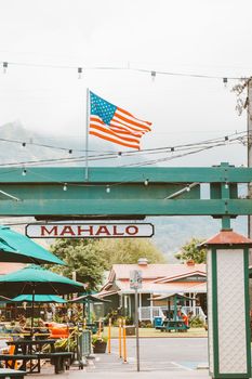 Photo by Jess Loiterton Quaint Hawaiian street scene featuring a US flag and a welcoming 'Mahalo' sign.