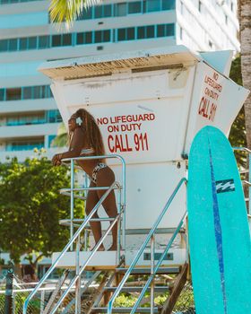 Woman in bikini at lifeguard tower by the city beach, embodying leisure and vacation.