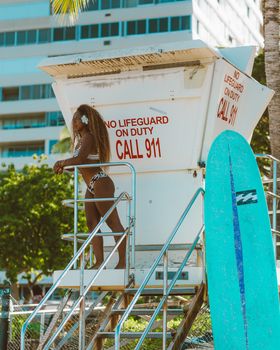 Beach view with lifeguard tower, woman in swimsuit, and surfboard.