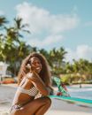 Smiling Woman in Bikini Crouching and Holding Surfboard 