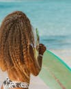 一位卷发女子拿着冲浪板，在阳光明媚的海滩上享受夏日的背影
