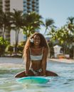 Portrait of a Woman Sitting on a Surfboard by a City Beach