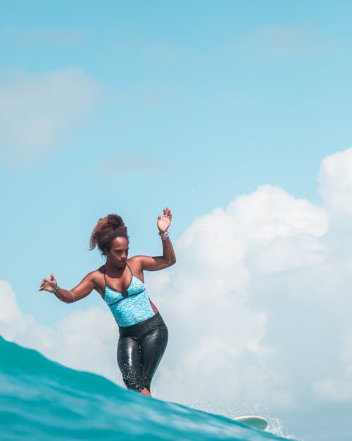 Woman in Blue Sports Bra and Black Pants Jumping Under Blue Sky