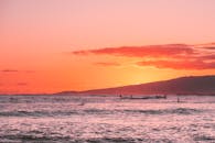 轮廓冲浪者在海洋上充满活力的日落中捕捉海浪，创造出宁静而风景如画的场景