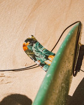 Close-up of a surfboard with a colorful floral fin on sandy beach. Summer vibes.