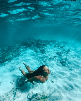 一名女子在清澈的蓝色海水中平静地享受水下自由潜水