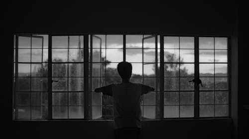 Silhouette of a Person Standing in Front of a Window