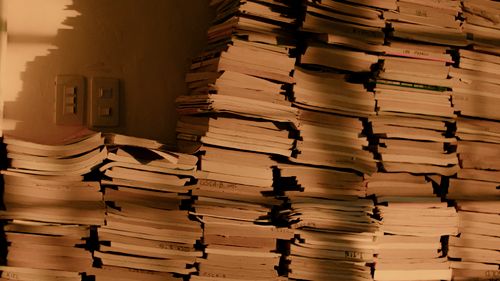 Free Stacks of old books and papers in shadowy light, suggesting a vintage or historical feel. Stock Photo