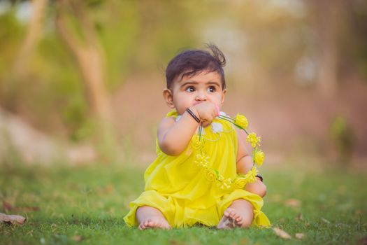 Cute baby girl sitting on grass in a yellow dress, playing with flowers. Captured outdoors in a natural setting.