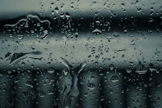 Moody image of raindrops on a glass window with blurred background.