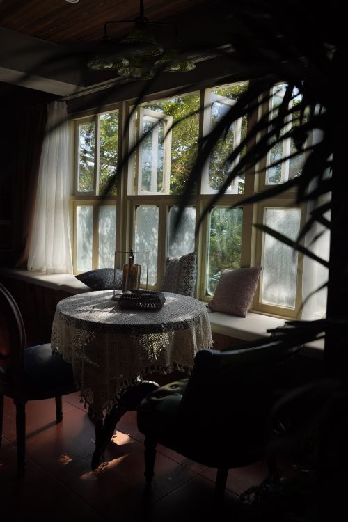 Free Elegant indoor dining setup with vintage chairs and lace tablecloth by sunny windows. Stock Photo