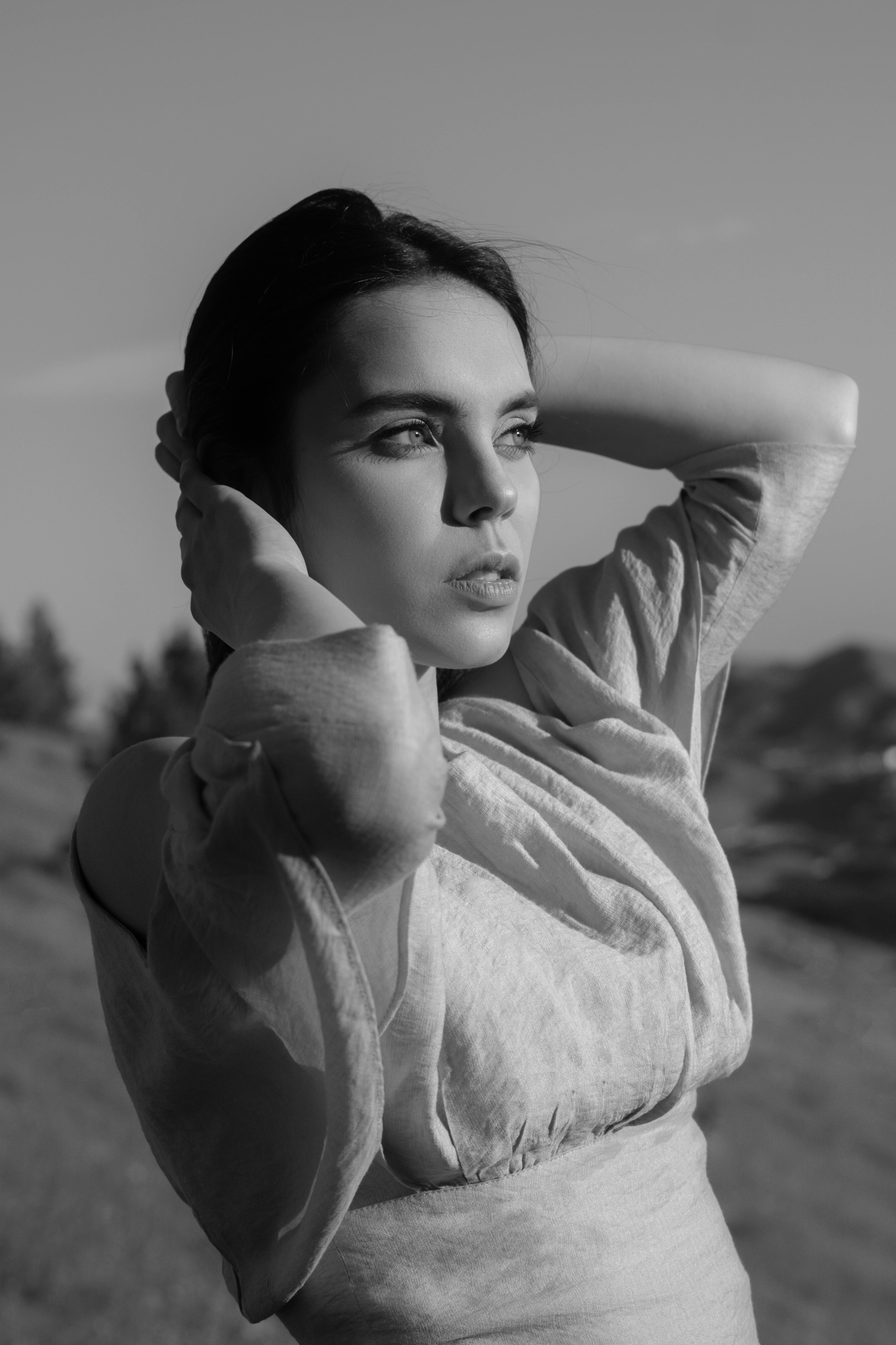 Black and white of pensive serious female in trendy summer dress looking away on blurred background of nature