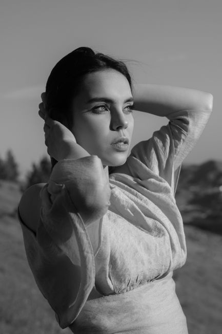 Black and white of pensive serious female in trendy summer dress looking away on blurred background of nature