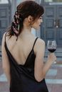一位时尚女士戴着围巾、穿着黑色连衣裙，正在户外享用葡萄酒