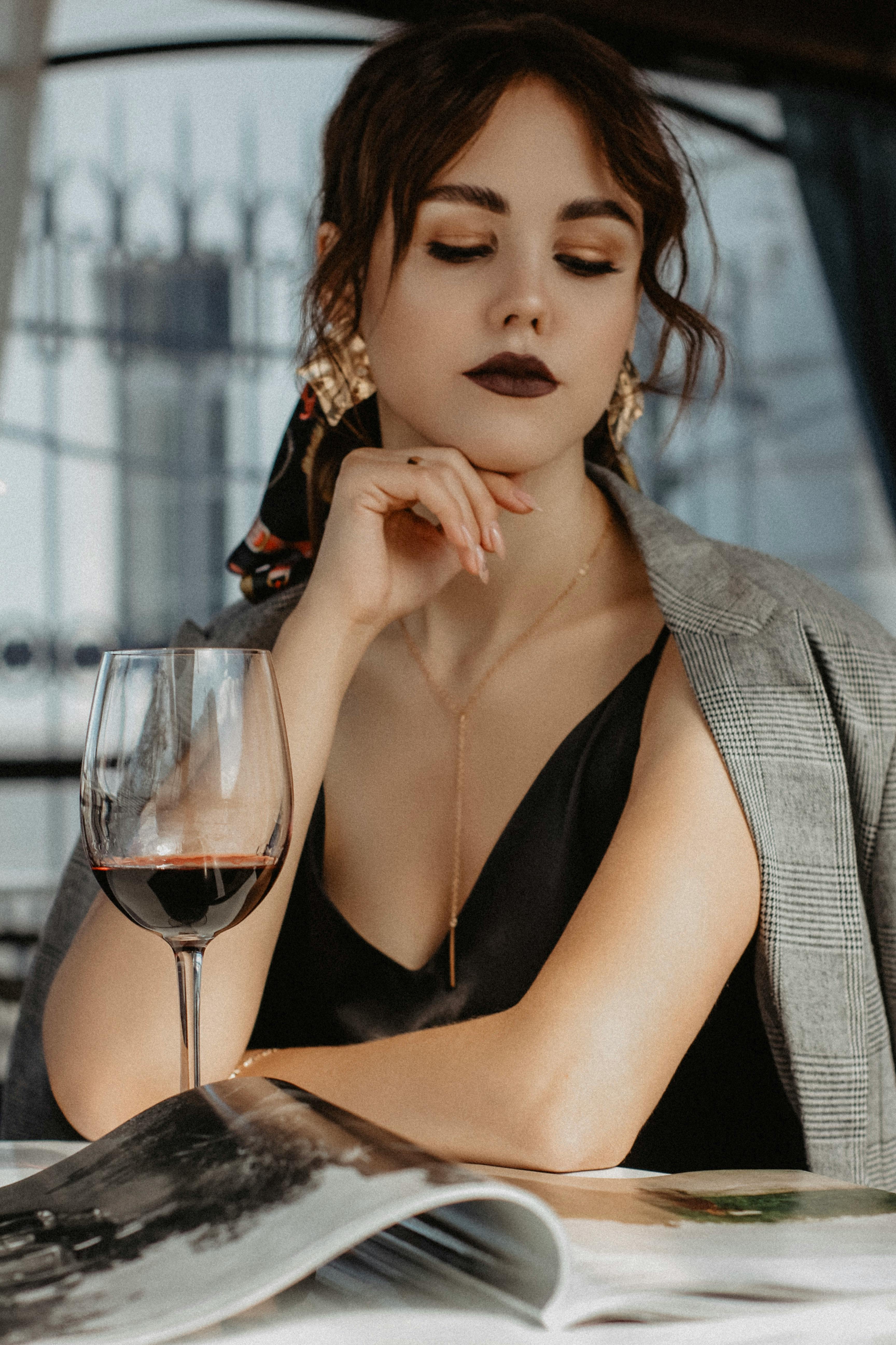 pensive young elegant female reading magazine and drinking wine in cafe