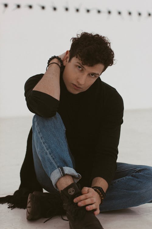 Serious young man sitting on floor and looking at camera pensively