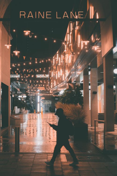 Free A silhouette of a person walking at night beneath vibrant street lights in Raine Lane, Perth, Australia. Stock Photo