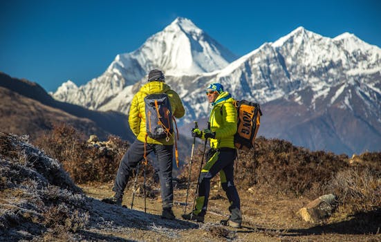 Two hikers enjoy a scenic trek in Mudi, with snowy peaks in the background.