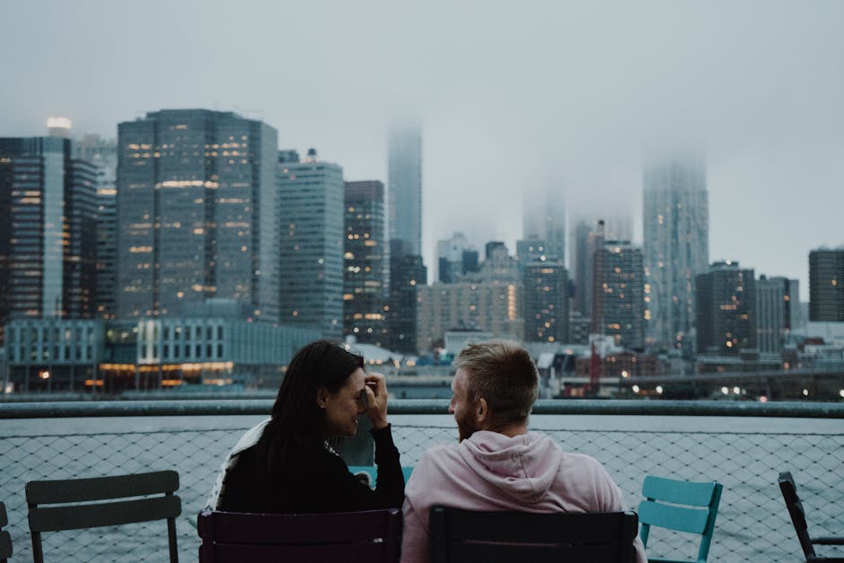 A couple enjoys a romantic moment with a foggy New York City skyline in the background.