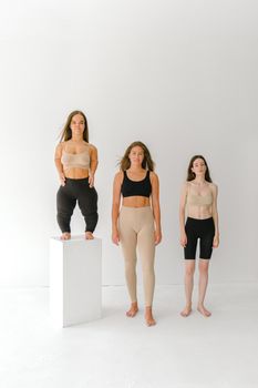 三位多元化女性身穿运动服，在工作室环境中拥抱身体积极性