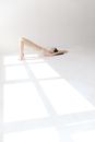 High angle side view of gorgeous young flexible female in leggings and top lying on floor with raised arms while performing variation of Setu Bandha Sarvangasana yoga pose