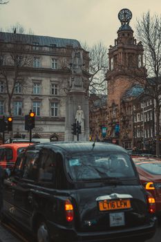 A classic London street scene featuring historic architecture and the iconic black cab, set against a moody sky.