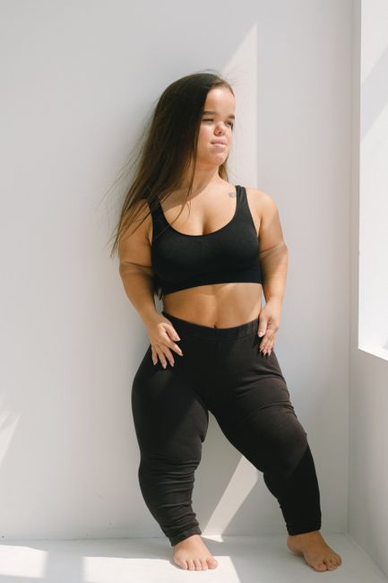 Confident woman with dwarfism posing in black activewear, embracing body positivity and empowerment.