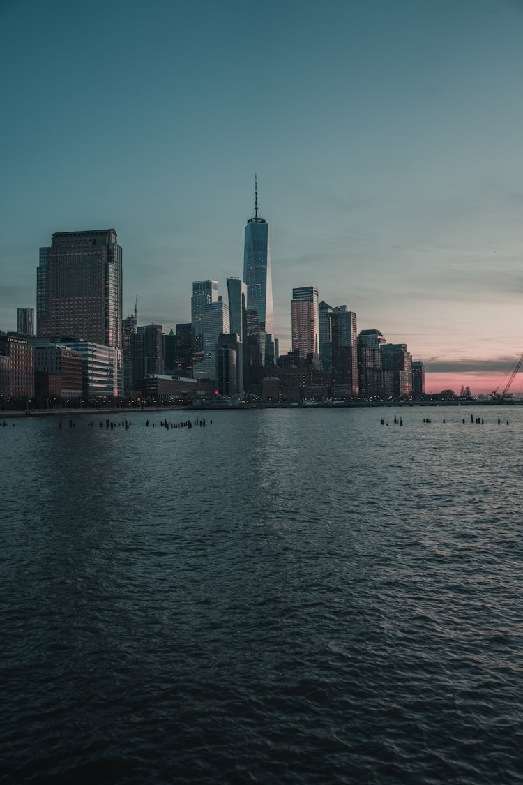 City Skyline With View Of One World Trade Center Across Body Of Water During Sunset