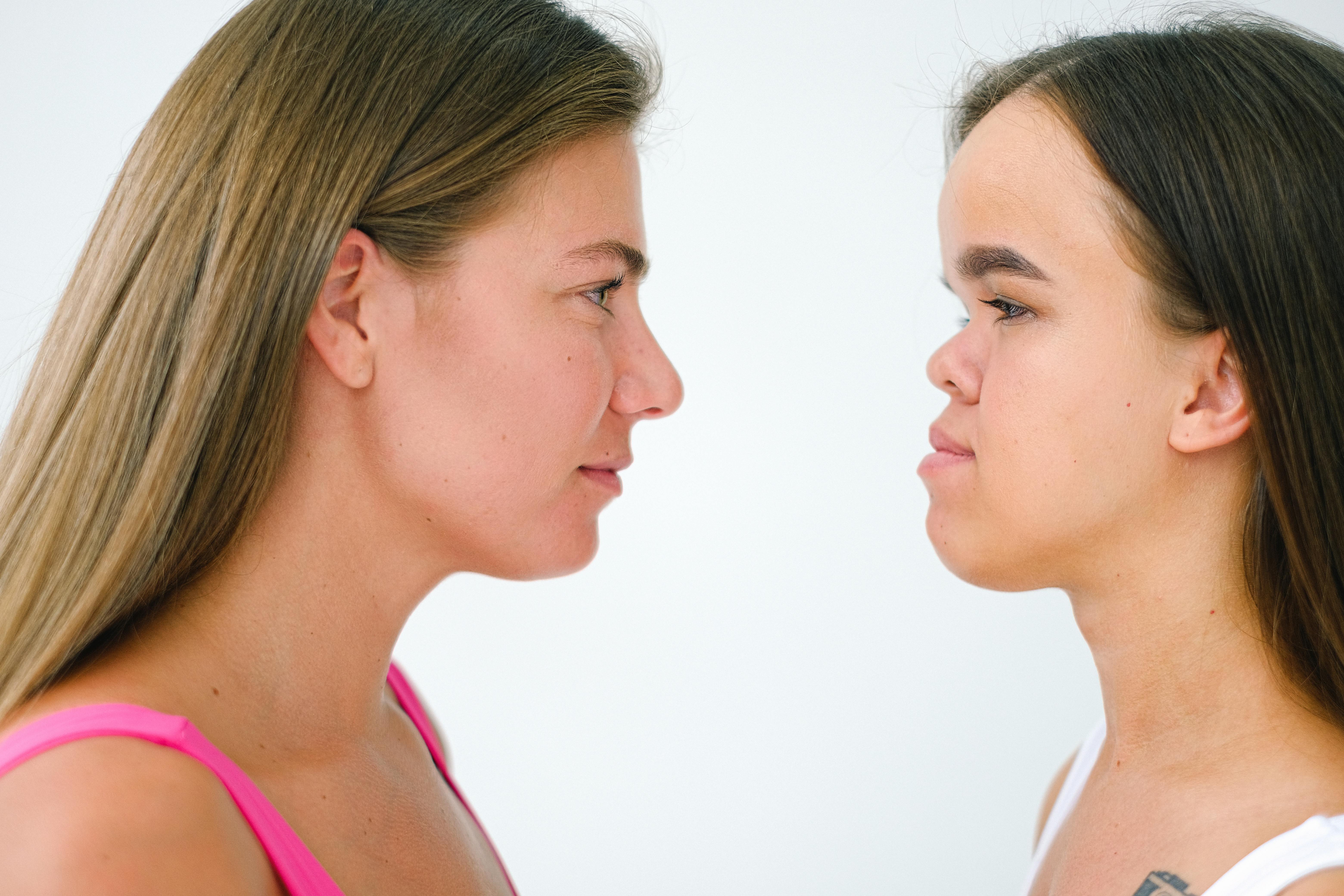 Close-up side profile of two women looking face to face against a white background.
