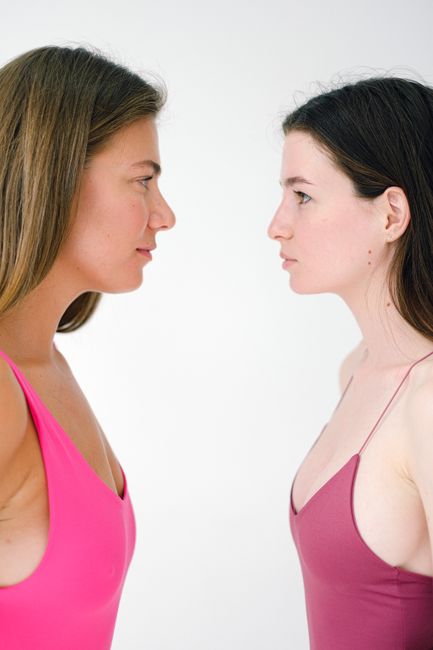 Side view of confident female wearing bright swimwear while standing face to face on white background and looking at each other