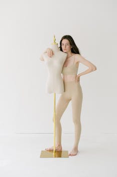Confident young woman in beige activewear poses with a mannequin indoors.
