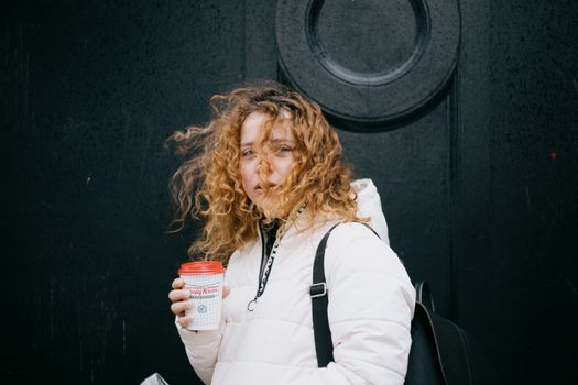 A woman with curly hair enjoying a warm coffee on a windy day in Glasgow.