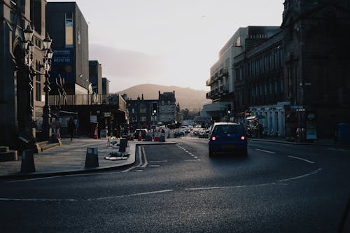 Cars Driving on Asphalt Road Between Buildings