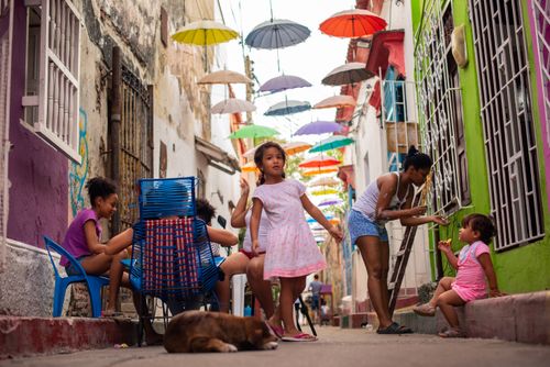 Free Colorful umbrellas and lively street scene in a Colombian neighborhood featuring kids and families. Stock Photo