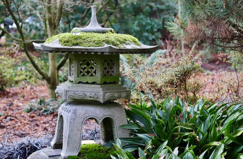Free A serene garden featuring a moss-covered stone lantern surrounded by lush greenery and plants. Stock Photo