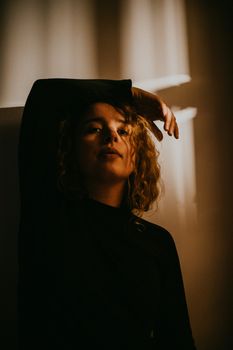 A woman poses dramatically, bathed in dim shadows indoors.