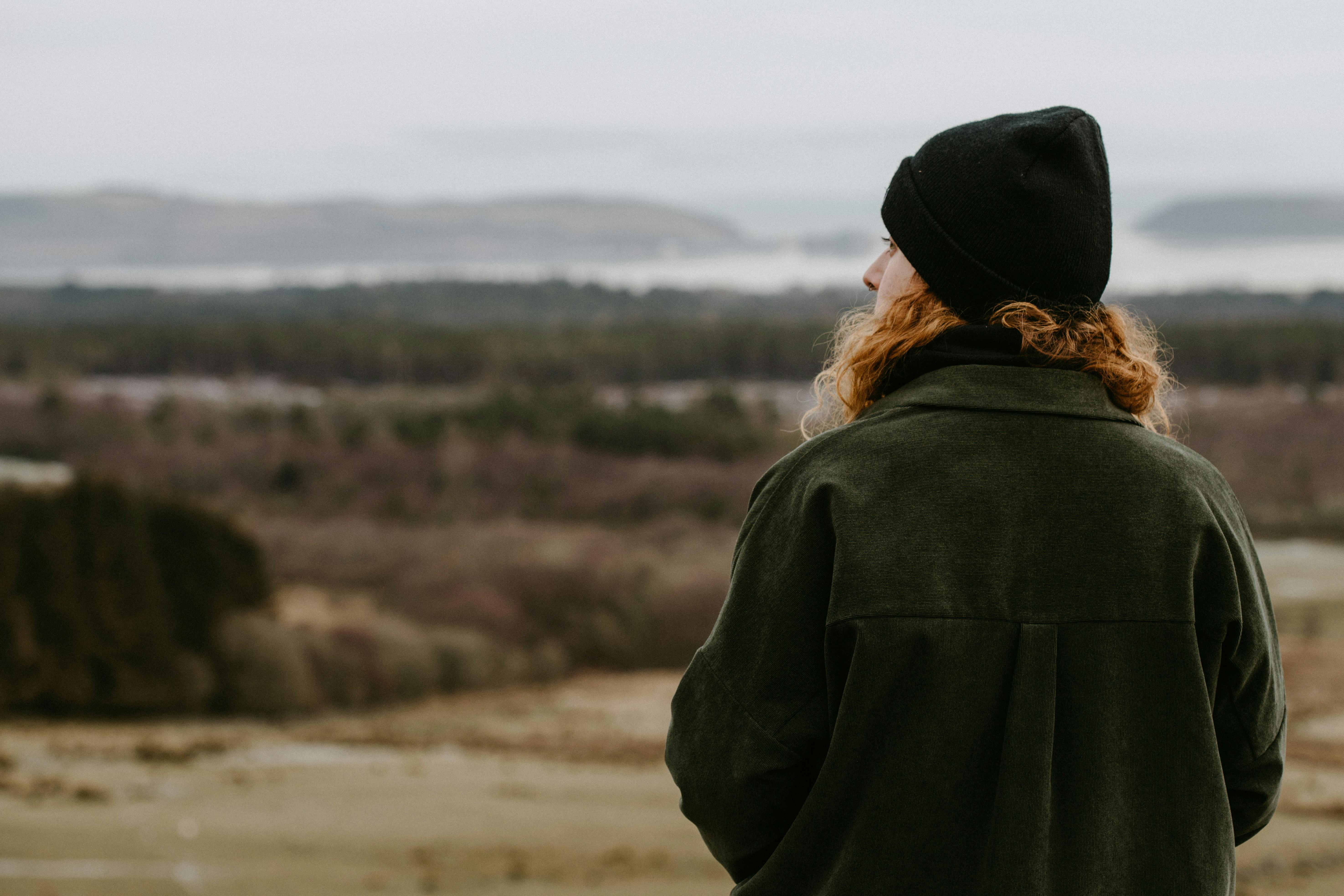A woman in a beanie gazes at a vast landscape in Inchindown, Scotland, evoking wanderlust and exploration.