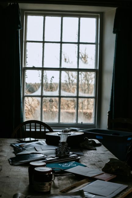 A cozy interior showcasing a mandolin on a messy table lit by natural light from a window.