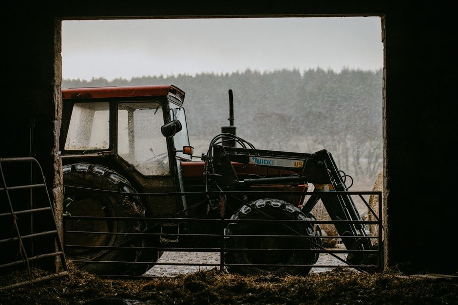 A vintage tractor parked in a rural Scottish farm shed with a scenic background.