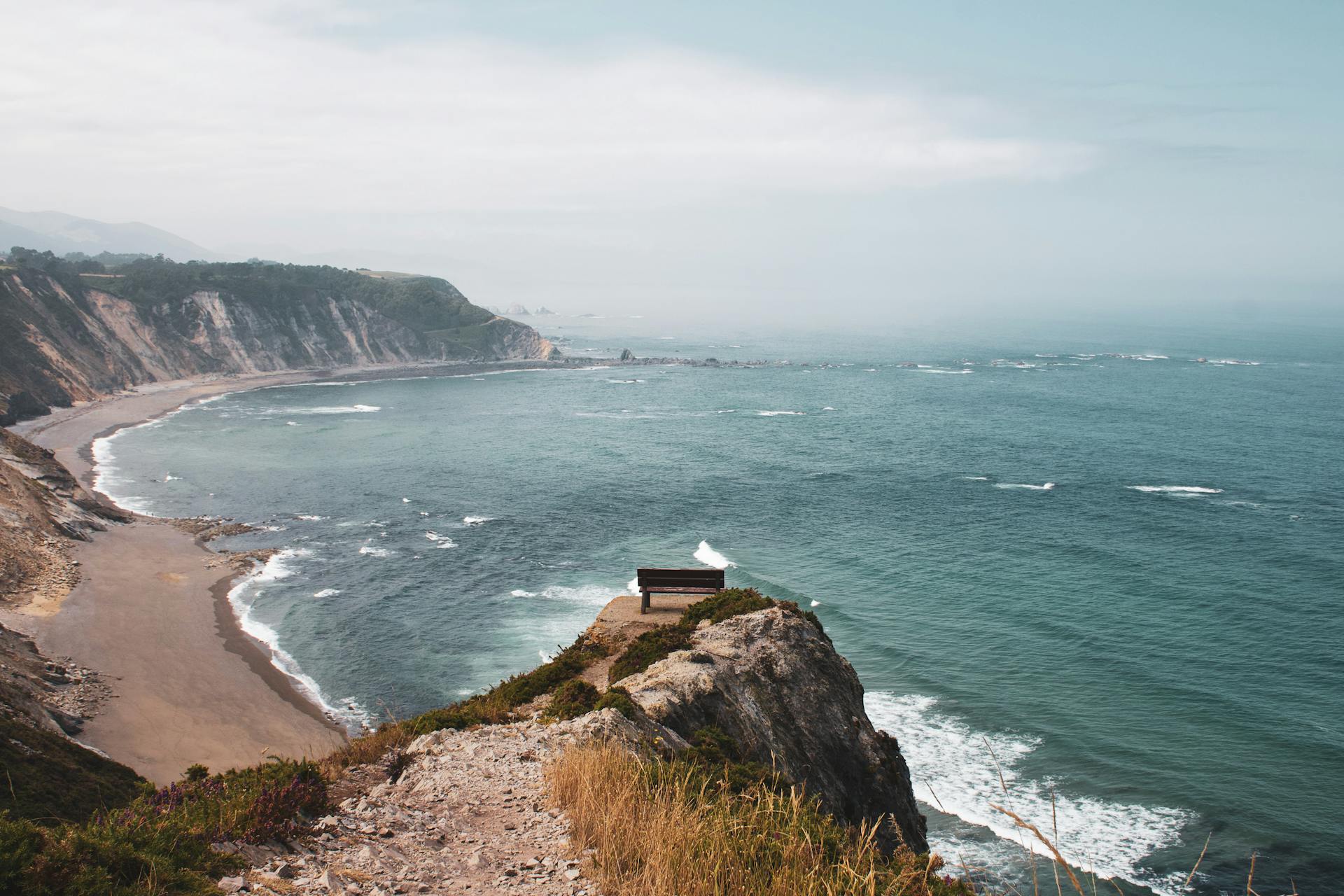 Breathtaking view of Asturias coastline from a cliff with a bench overlooking the Cantabrian Sea.