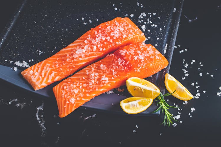 Raw Pieces Of Salmon With Salt And Lemon Wedges On A Baking Tray