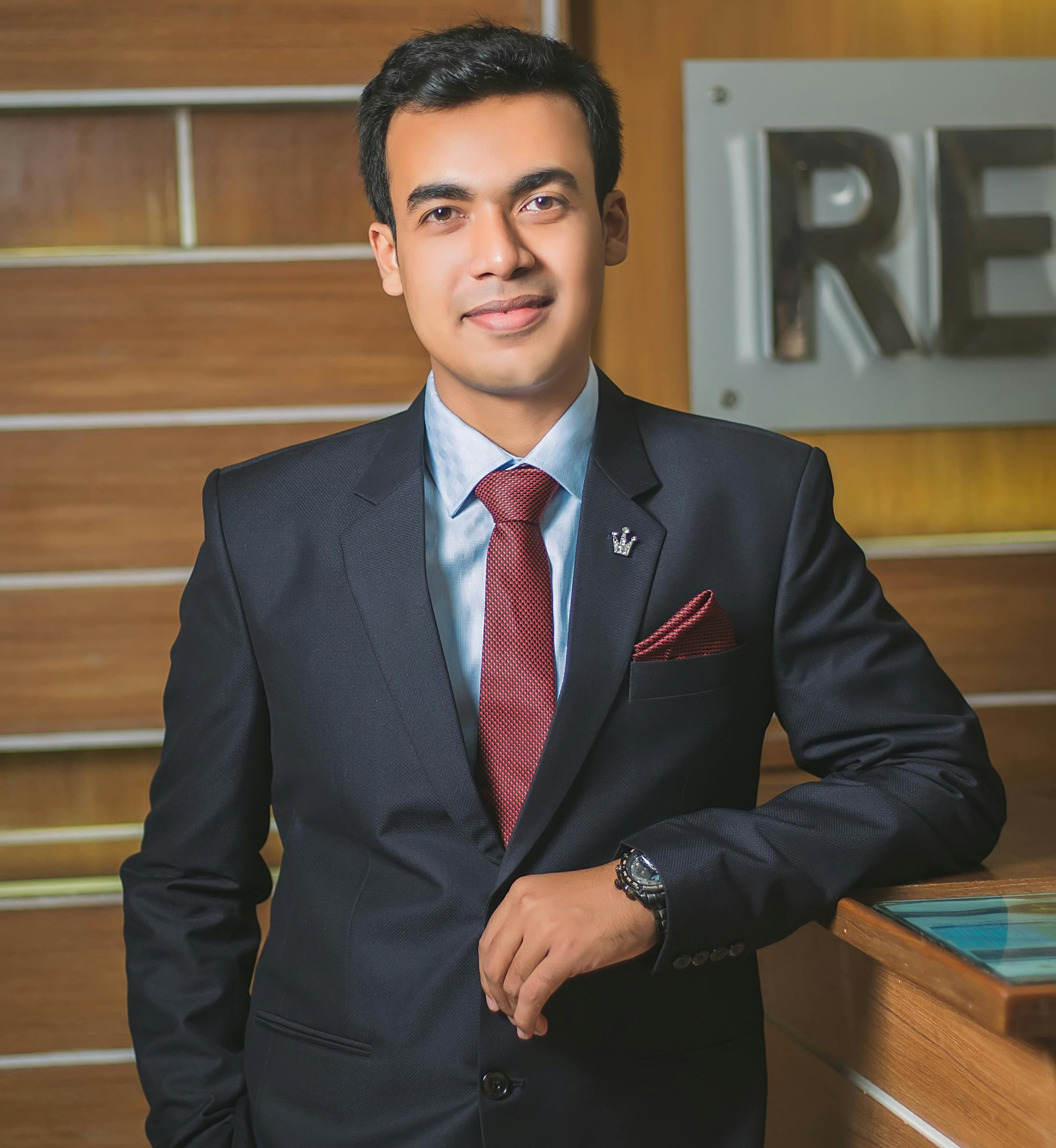 A confident young professional man in a suit posing indoors with a smile.