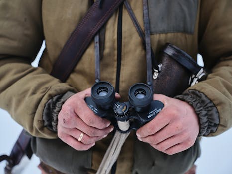 A person in a jacket holds binoculars outdoors, emphasizing adventure and exploration.